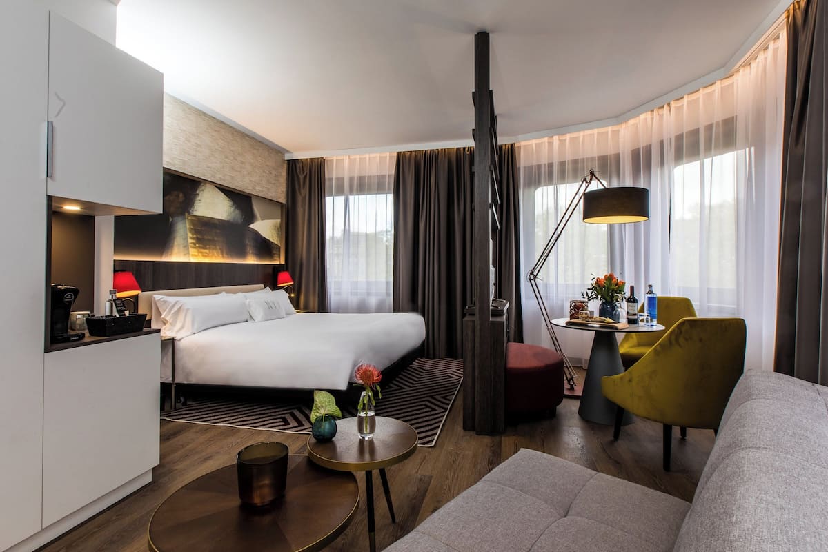 Moderni hotellihuone, jossa on sänky, työpöytä, sohva ja ruokailutila.