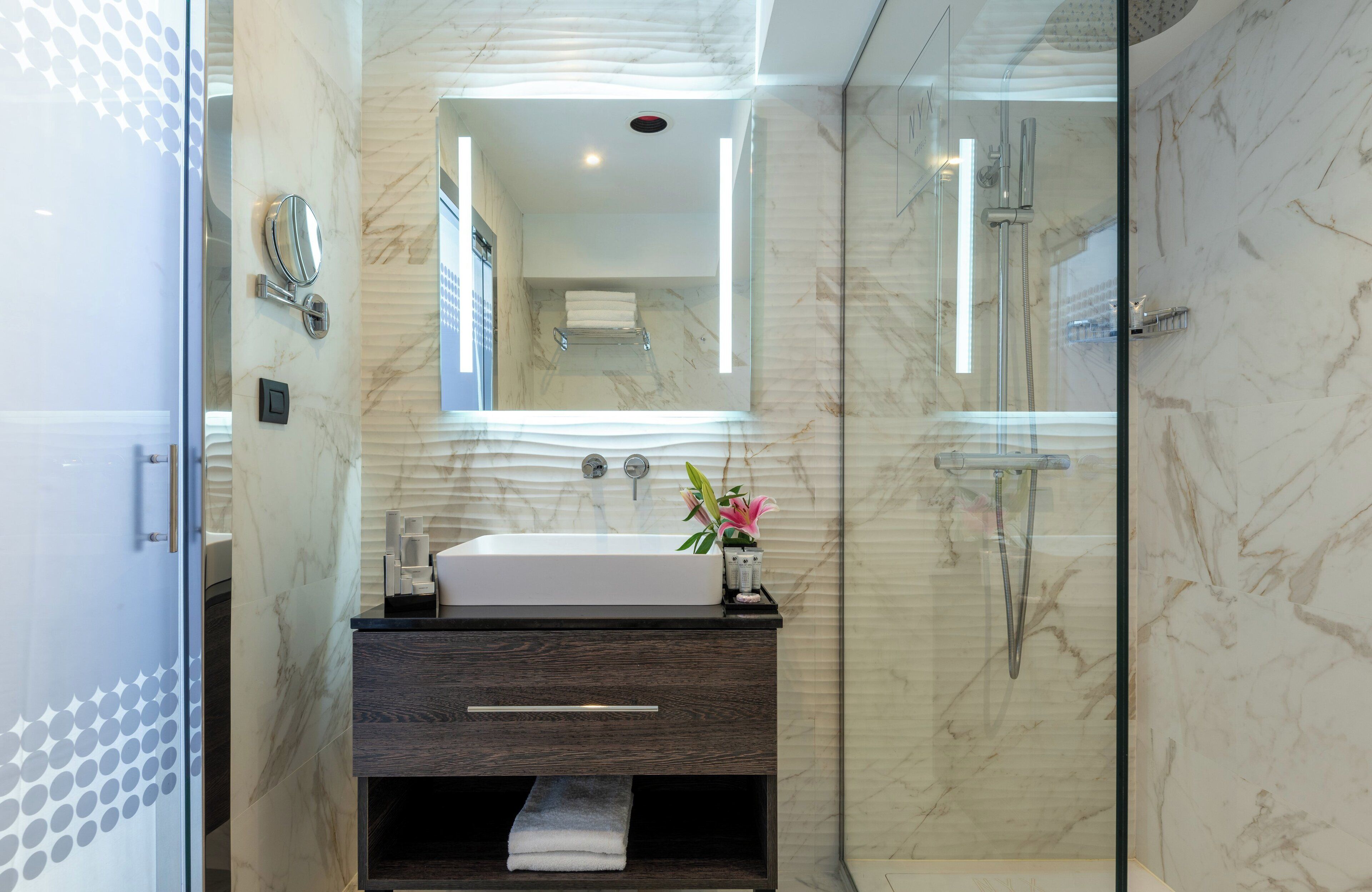 Un bagno moderno con doccia vetro, lavabo in marmo e mobile vanitario in legno scuro.