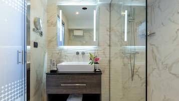 Un bagno moderno con doccia vetro, lavabo in marmo e mobile vanitario in legno scuro.