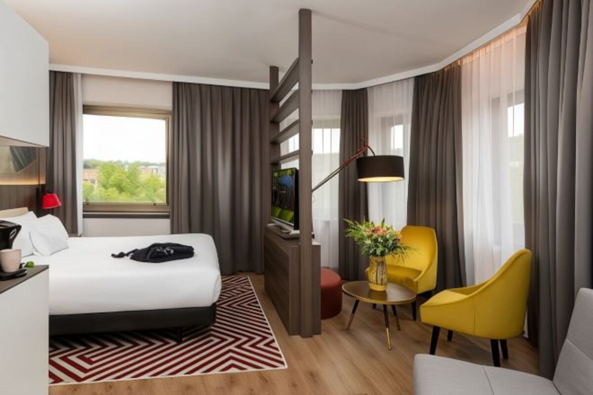 A hotel room with a bed, a desk, a chair, a TV, and a window with curtains.