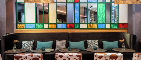 A modern lounge area with a black sofa, patterned ottomans, and round tables.
