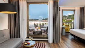 A modern hotel room with a balcony, a sofa, a dining table, and a bed. - NYX Hotel Bilbao by Leonardo Hotels (Bilbao)