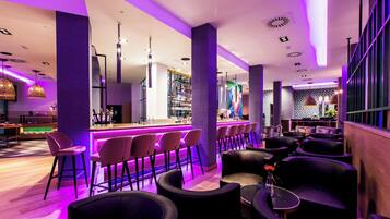 A modern bar area with purple lighting, bar stools, and a counter.