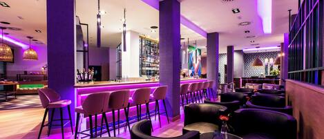 A modern bar area with purple lighting, bar stools, and a counter.