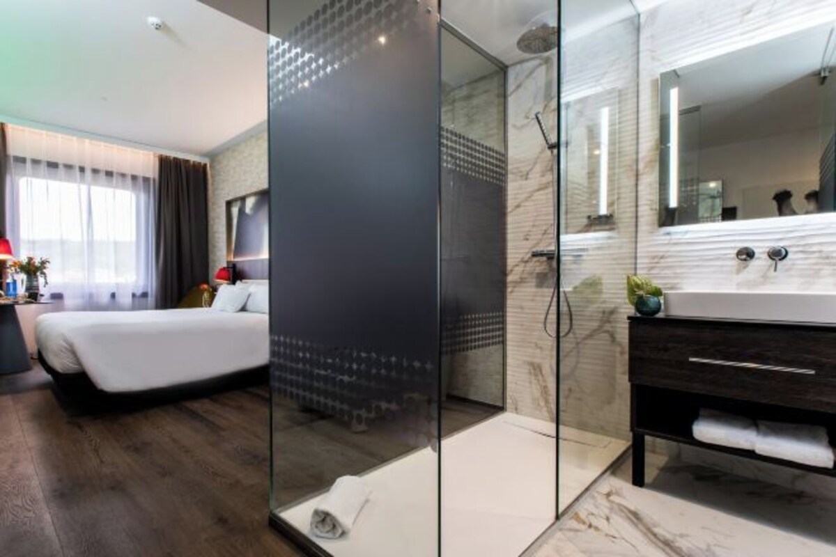 A modern hotel room with a large bed, a glass-enclosed shower, a marble bathroom, and a large mirror.