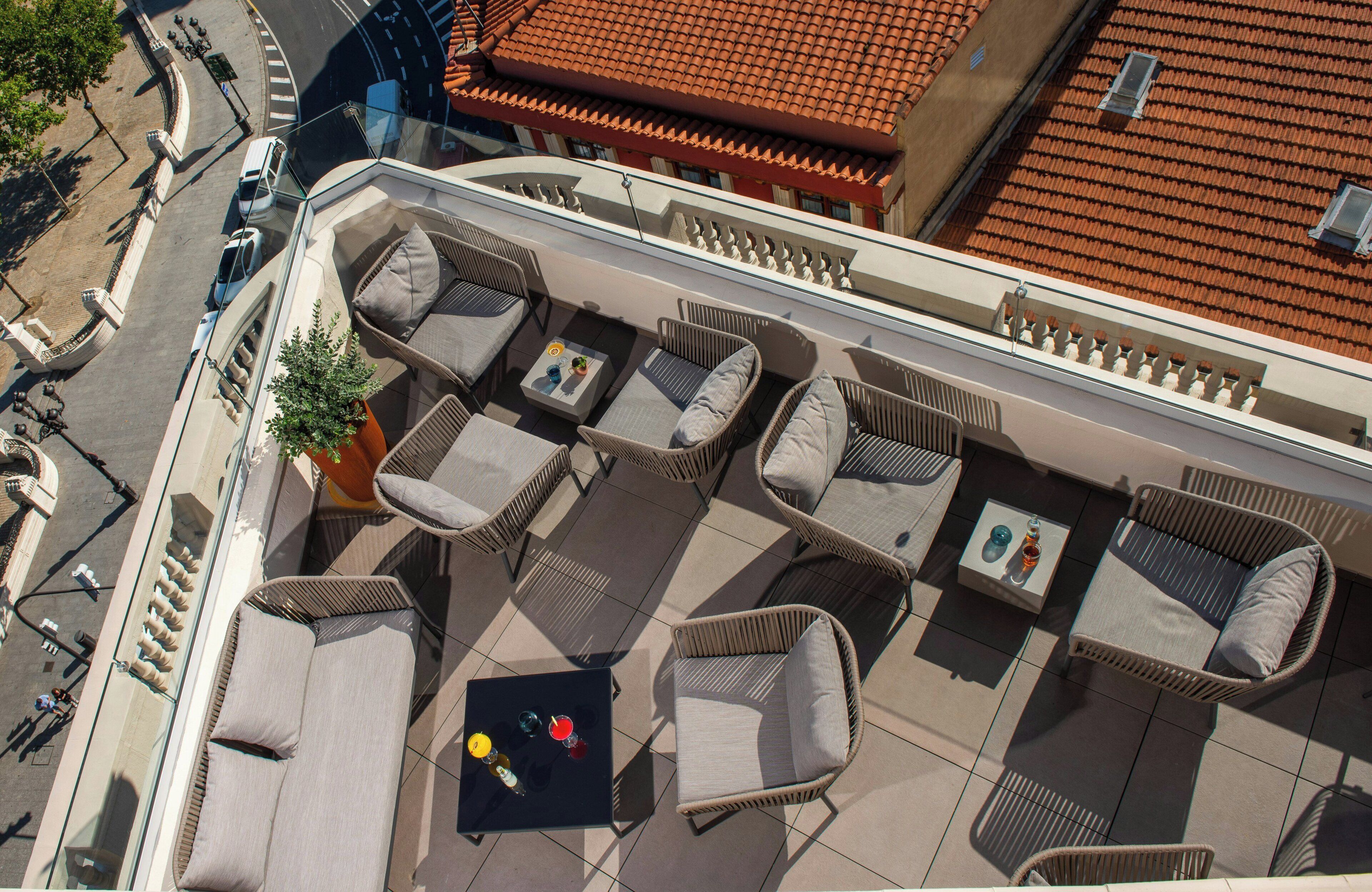 Un área de estar al aire libre con muebles de mimbre y una pequeña mesa, con vista a una calle de la ciudad.