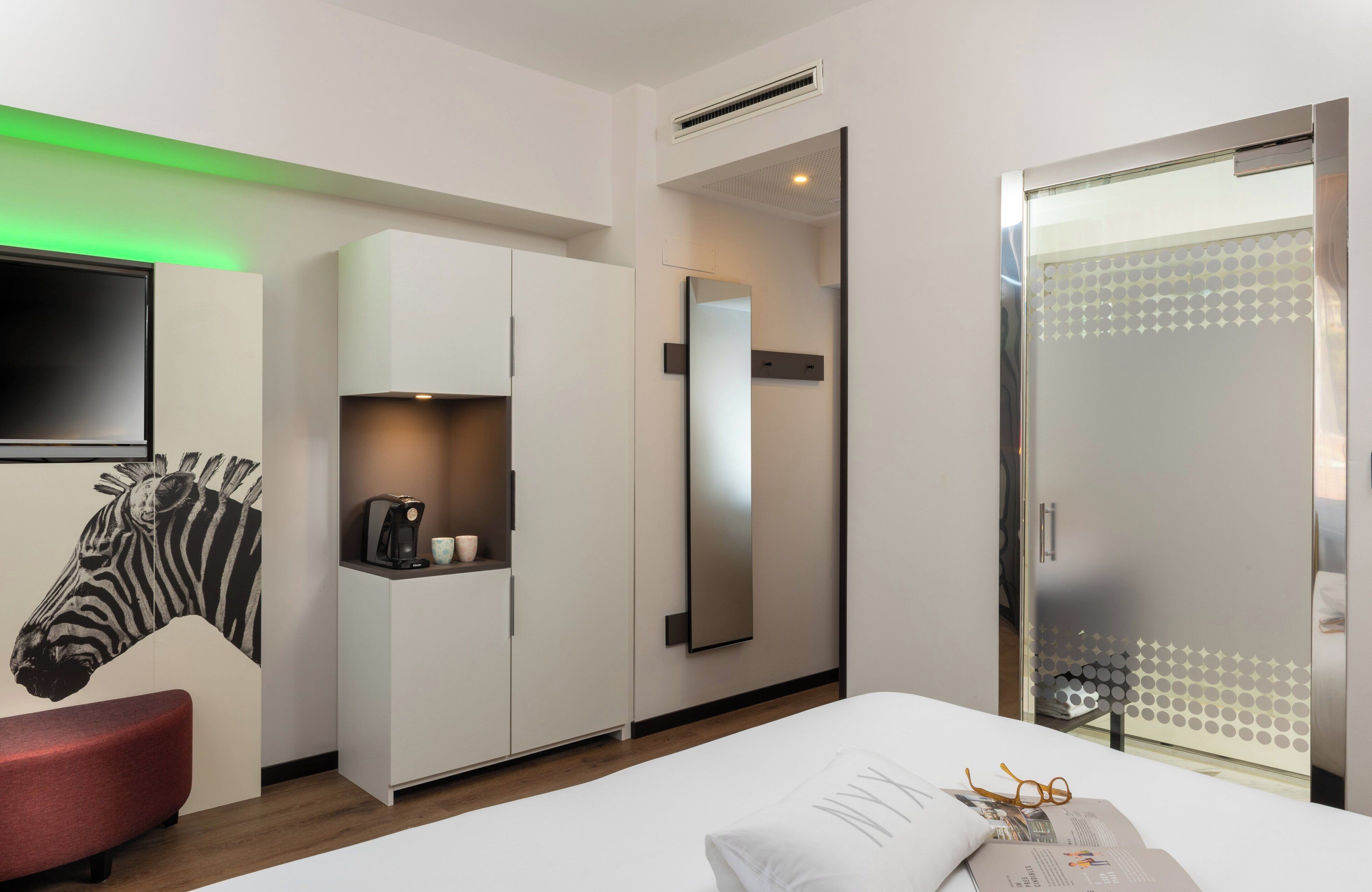 Een moderne hotelkamer met een groot bed, een garderobe, een spiegel en een muurschildering van een zebra op de wand.