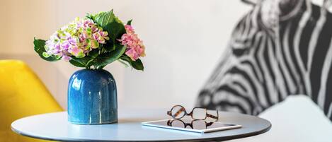 A blue vase with pink flowers on a round table, glasses, and a notebook.