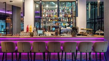 Zona de bar con mostrador iluminado en morado, varias botellas de licor y taburetes.