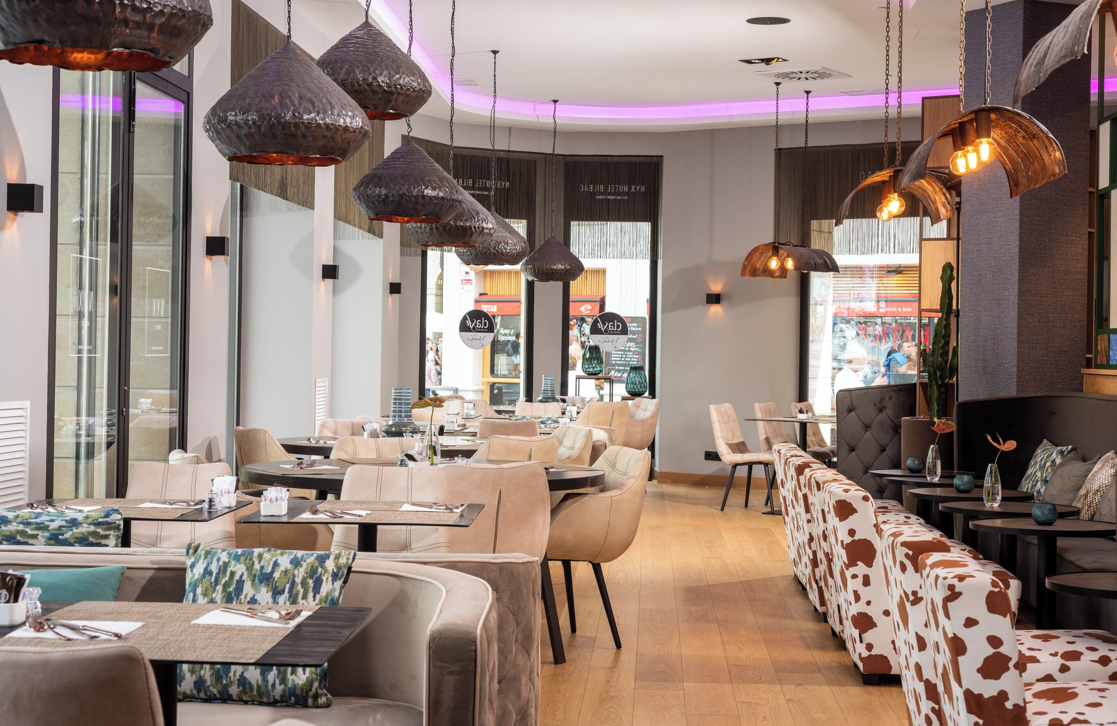 A modern restaurant interior with high tables, cushioned seating, and pendant lighting.