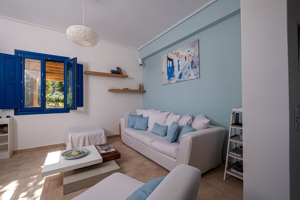 A modern living room with a white sofa, blue cushions, a coffee table, and a painting on the wall. - Santorini Mystique Garden (Santorini)