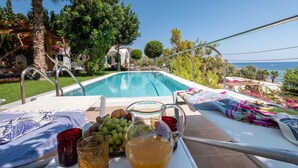 Ein Poolbereich mit Liegestuhl, Tisch mit Limonadenglas und Blick aufs Meer.
