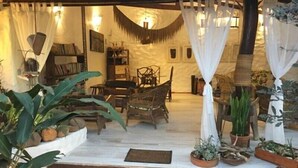 A cozy, rustic interior with a wooden dining table, chairs, and a bookshelf. White curtains and plants add to the ambiance. - Pousada Bambu Brasil (Alto Paraíso de Goiás)