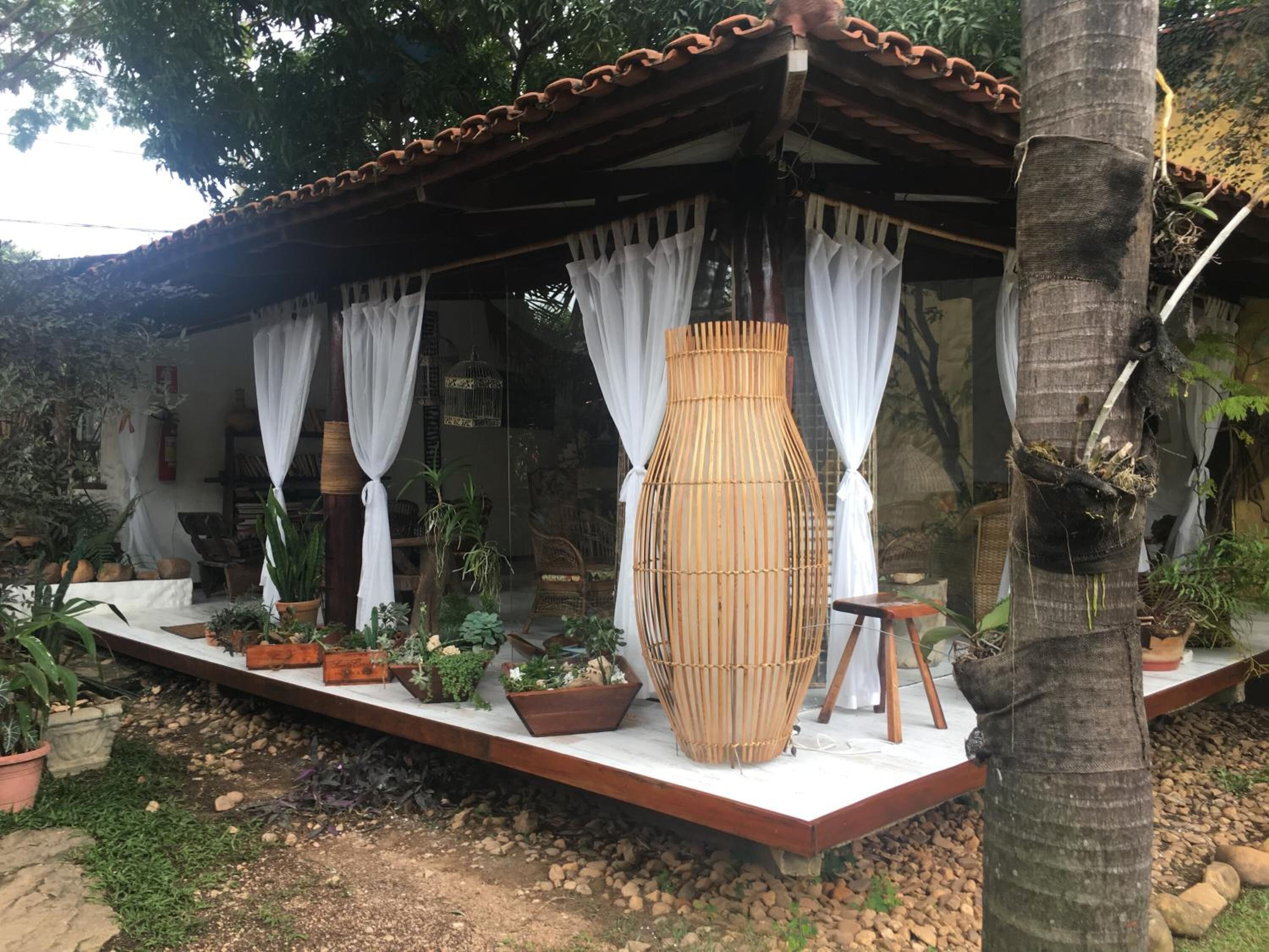 A covered outdoor seating area with a wooden bench, potted plants, and a large bamboo basket.