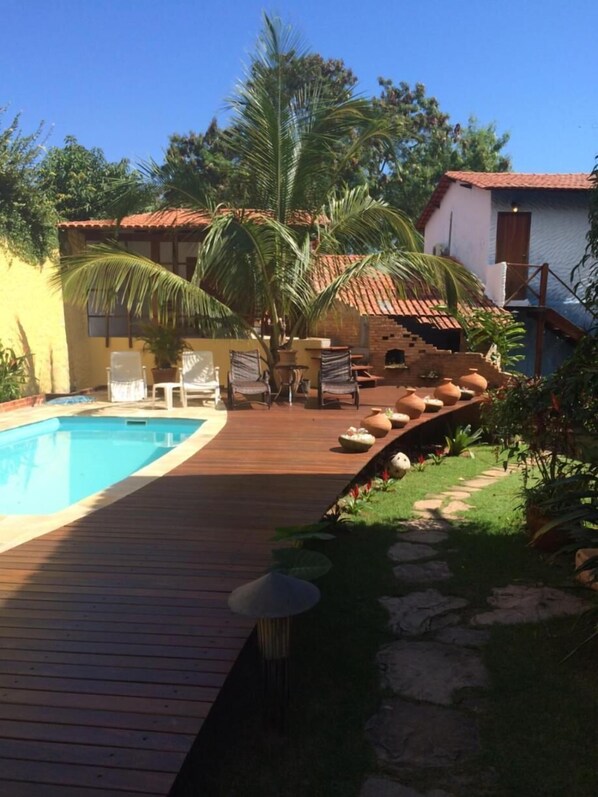 A wooden deck leading to a swimming pool, surrounded by palm trees and a small garden area with a stone pathway.