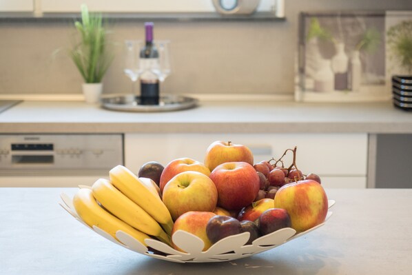 Un panier de fruits posé sur un plan de travail de cuisine, contenant des bananes, des pommes et des raisins.