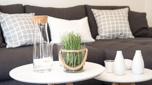 A modern living room with a white round table, a glass vase with green plants, and white vases on a small side table. - Miralior Apartment (Mainz)