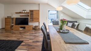 A modern living room with a wooden dining table, black chairs, a TV, and a large window. - Miralior Apartment (Mainz)