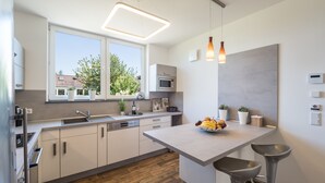 A modern kitchen with white cabinets, a wooden floor, a large window, and a fruit bowl on the island. - Miralior Apartment (Mainz)