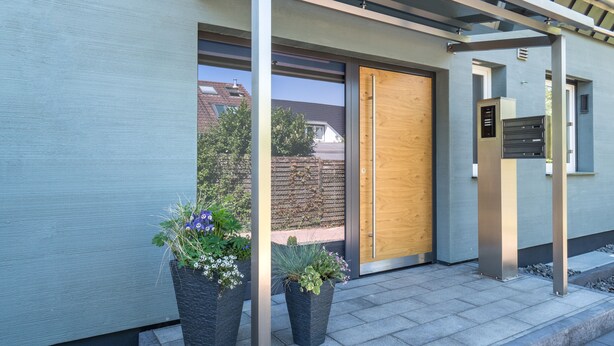 A modern building entrance with a wooden door, metal pillars, and potted plants. - Miralior Apartment (Mainz)