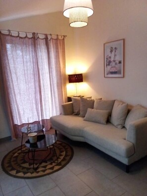 Uma sala de estar com um sofá bege, uma mesa de centro redonda, um abajur e um quadro na parede.