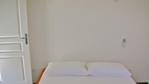Una habitació senzilla amb un llit, una porta blanca i una làmpada penjada a la paret.