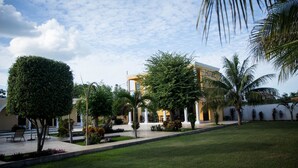 A hotel with a well-maintained lawn, palm trees, and a clear sky. - Hotel Hacienda Izamal (Izamal)
