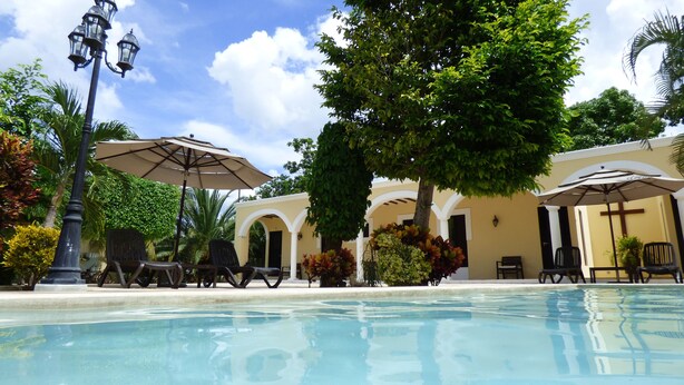 A poolside area with lounge chairs, umbrellas, and a building with arches. - Hotel Hacienda Izamal (Izamal)
