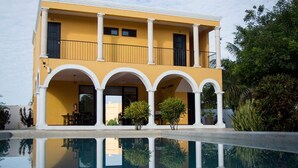 A two-story building with a yellow facade and white columns, featuring a pool with a clear reflection. - Hotel Hacienda Izamal (Izamal)