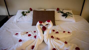 Un lit bien fait, avec des draps blancs, un oreiller marron et un bouquet de roses rouges.