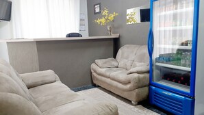 Una sala de estar con un sofá color beige, un refrigerador azul y una mesita con un jarrón de flores.