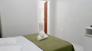 Habitación de hotel con cama, una manta verde, una toalla blanca, una puerta de madera y un estante blanco.