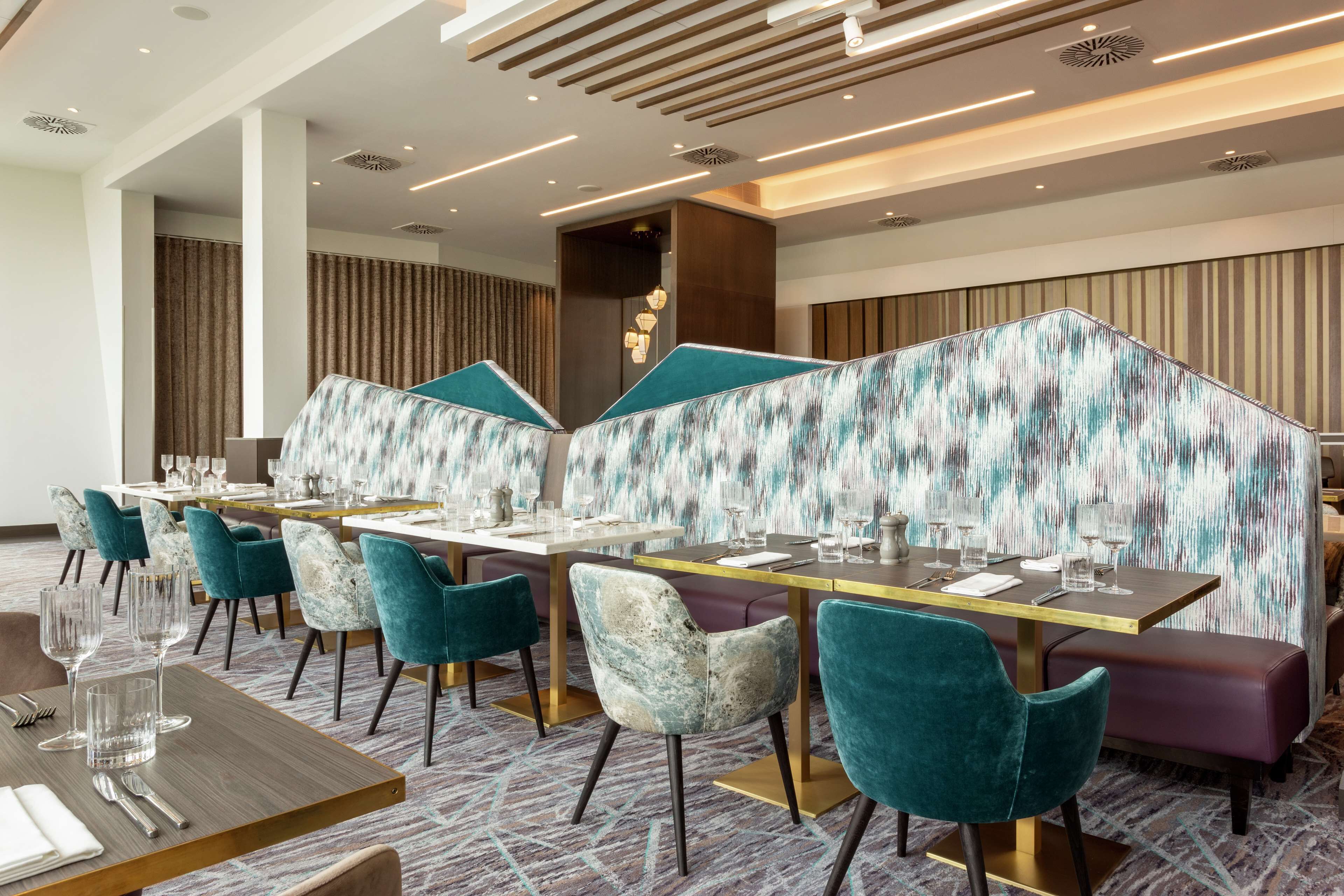 A modern dining area with teal and white upholstered chairs, a long table set for a meal, and a patterned wall divider.