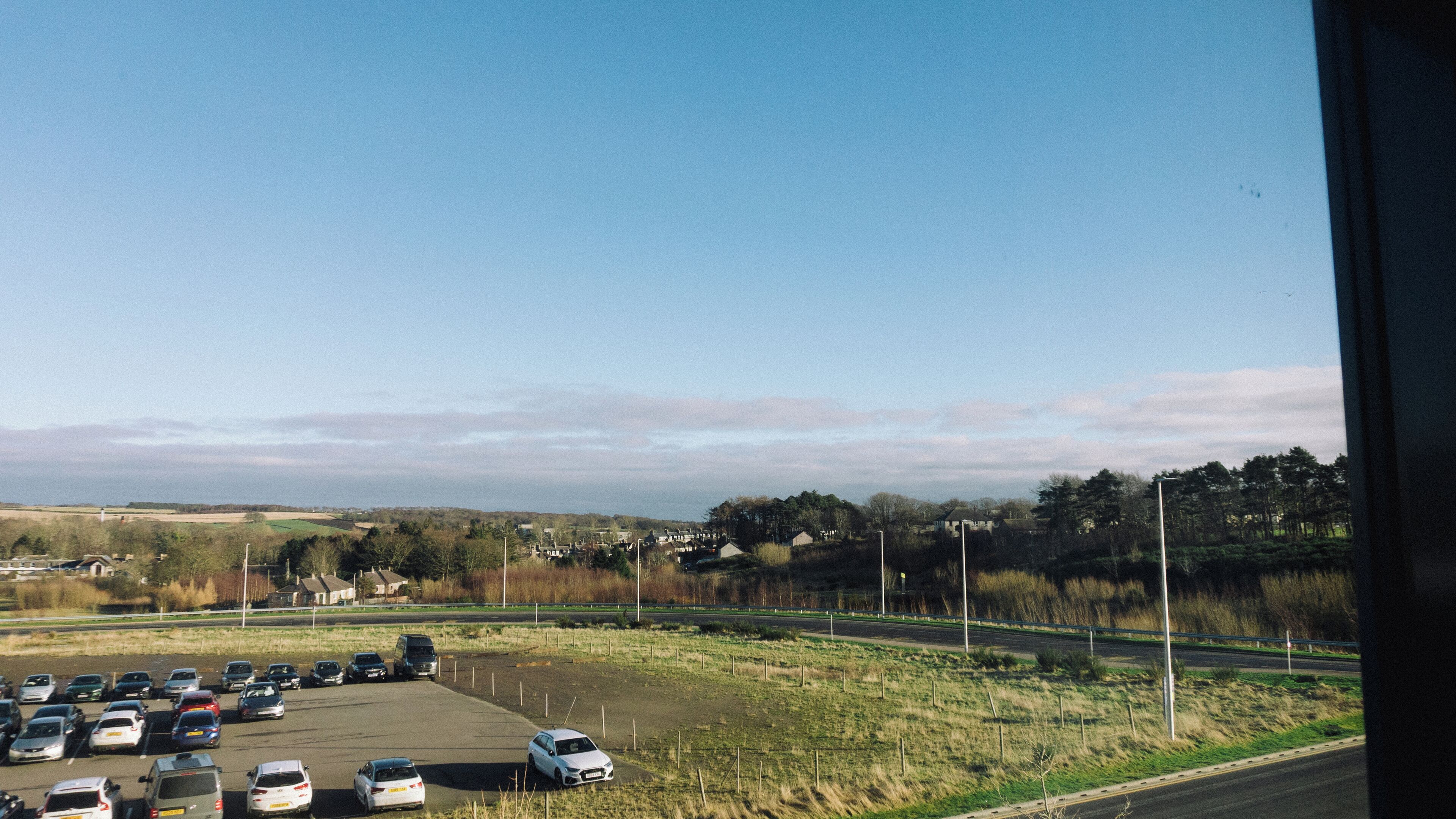 A parking lot with several cars and a road in the background.