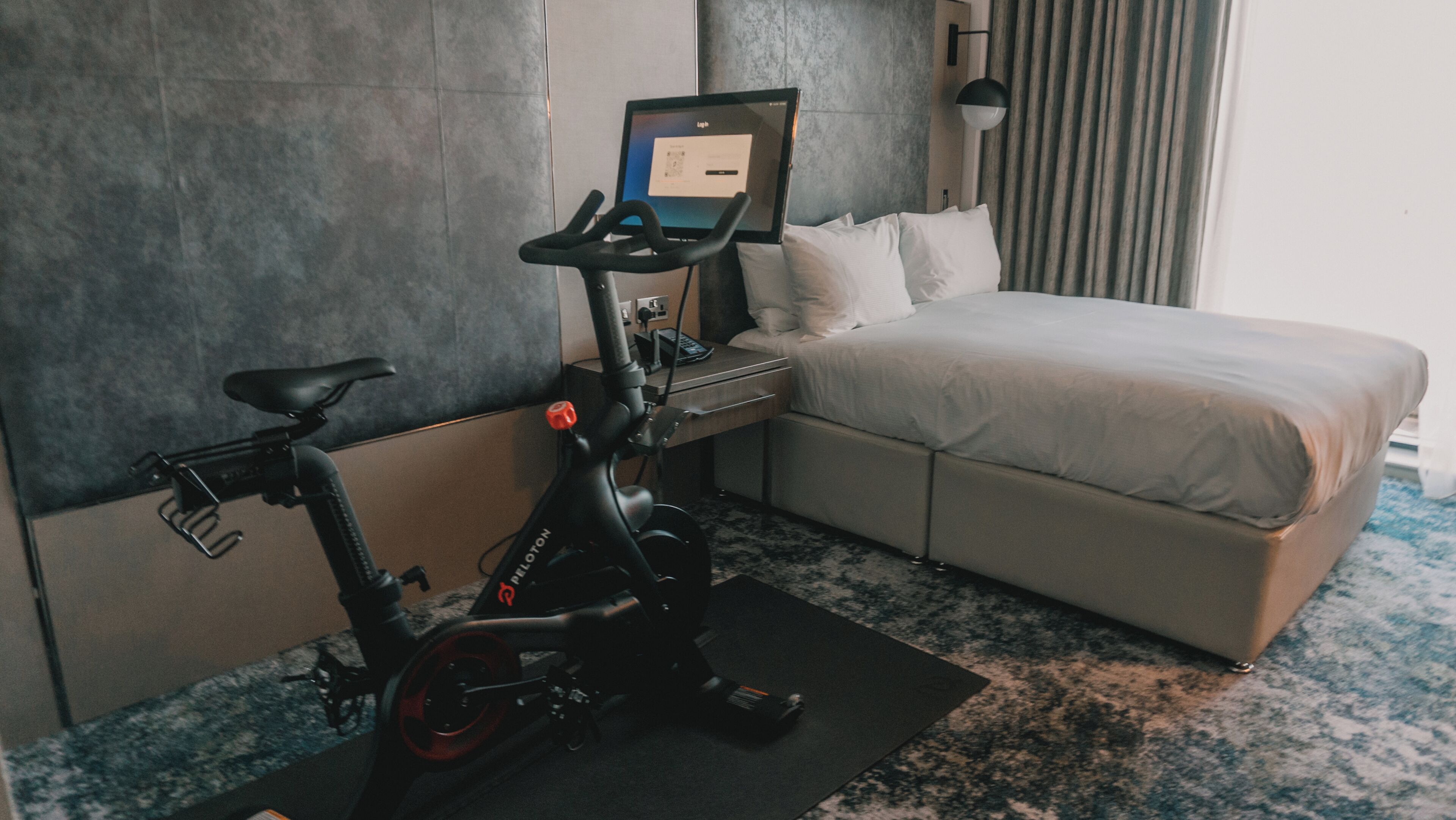 A hotel room with a bed, a desk with a laptop, and an exercise bike.
