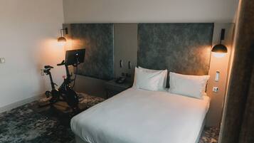 A hotel room with a large bed, a desk with a phone, a bike, and two wall-mounted lamps.