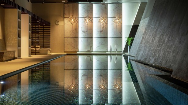 A modern indoor pool area with a clear glass floor, geometric wall designs, and a staircase with a unique pattern. - Hilton Aberdeen TECA (Aberdeen)