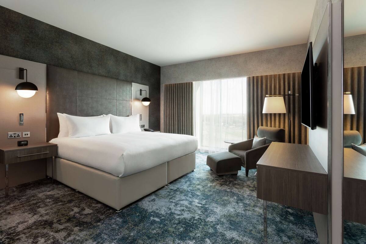Quarto de hotel moderno com uma cama grande, escrivaninha, cadeira e televisão.
