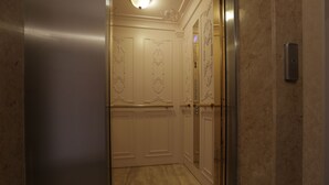 A modern elevator with a marble floor and wall, leading to a room with white doors and decorative moldings. - Luxury Apartment in Anastasia Palace (Sunny Beach)