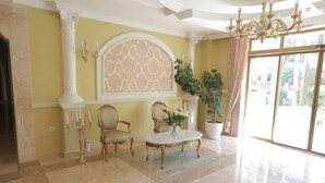 A spacious room with a marble floor, a large window with curtains, a chandelier, and two ornate chairs. - Luxury Apartment in Anastasia Palace (Sunny Beach)