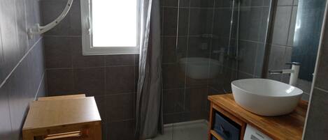 Une salle de bain moderne dotée d’une grande fenêtre, d’une douche à l’italienne, d’un lavabo et d’un meuble-vasque en bois.