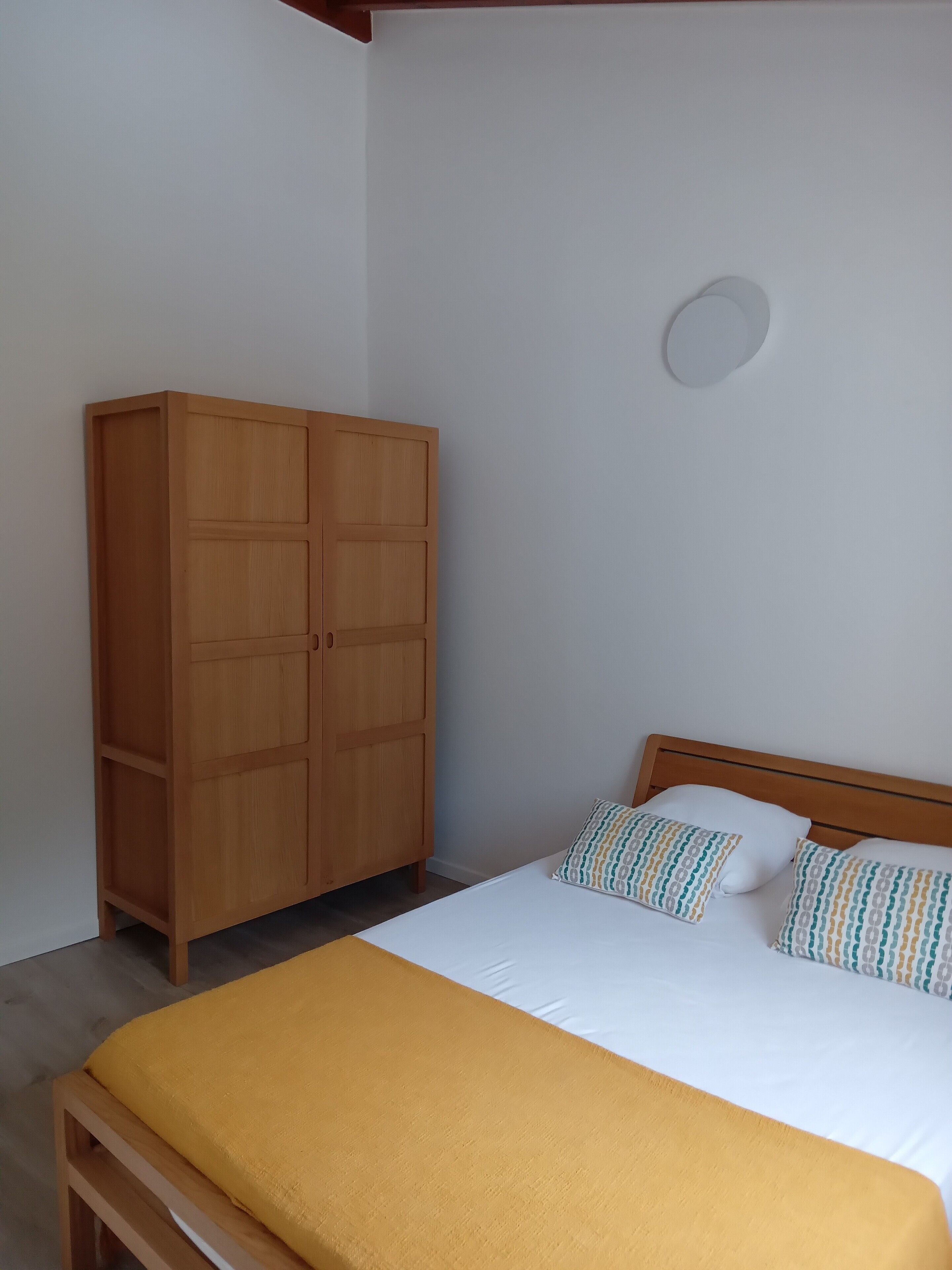 A bedroom with a bed, a wooden wardrobe, and a bedside table.