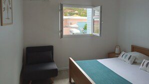 Une chambre à coucher avec un lit, une chaise, une fenêtre ouverte et un appareil de climatisation.