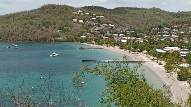 Une ville côtière avec une plage, des bateaux et des maisons situées sur une colline.