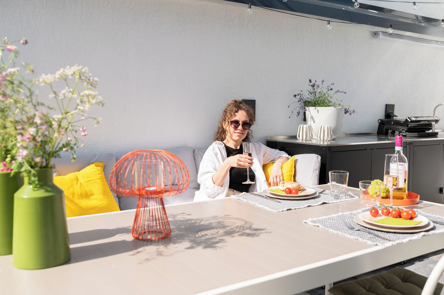 A dining area with a table set for two, featuring a bottle of wine, a plate with tomatoes, and a glass of water.