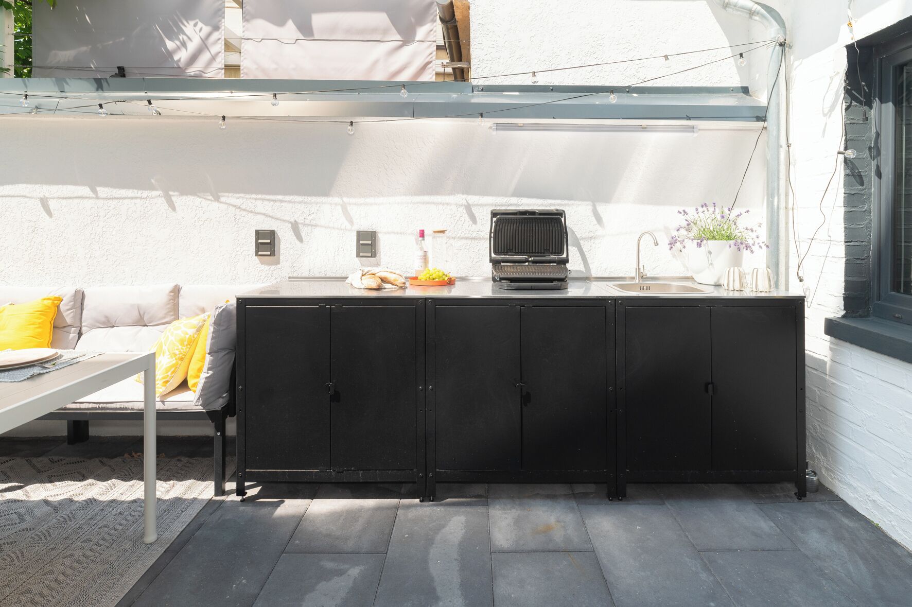 Une terrasse dotée d’un espace barbecue, de sièges extérieurs et offrant une vue sur la façade du bâtiment.