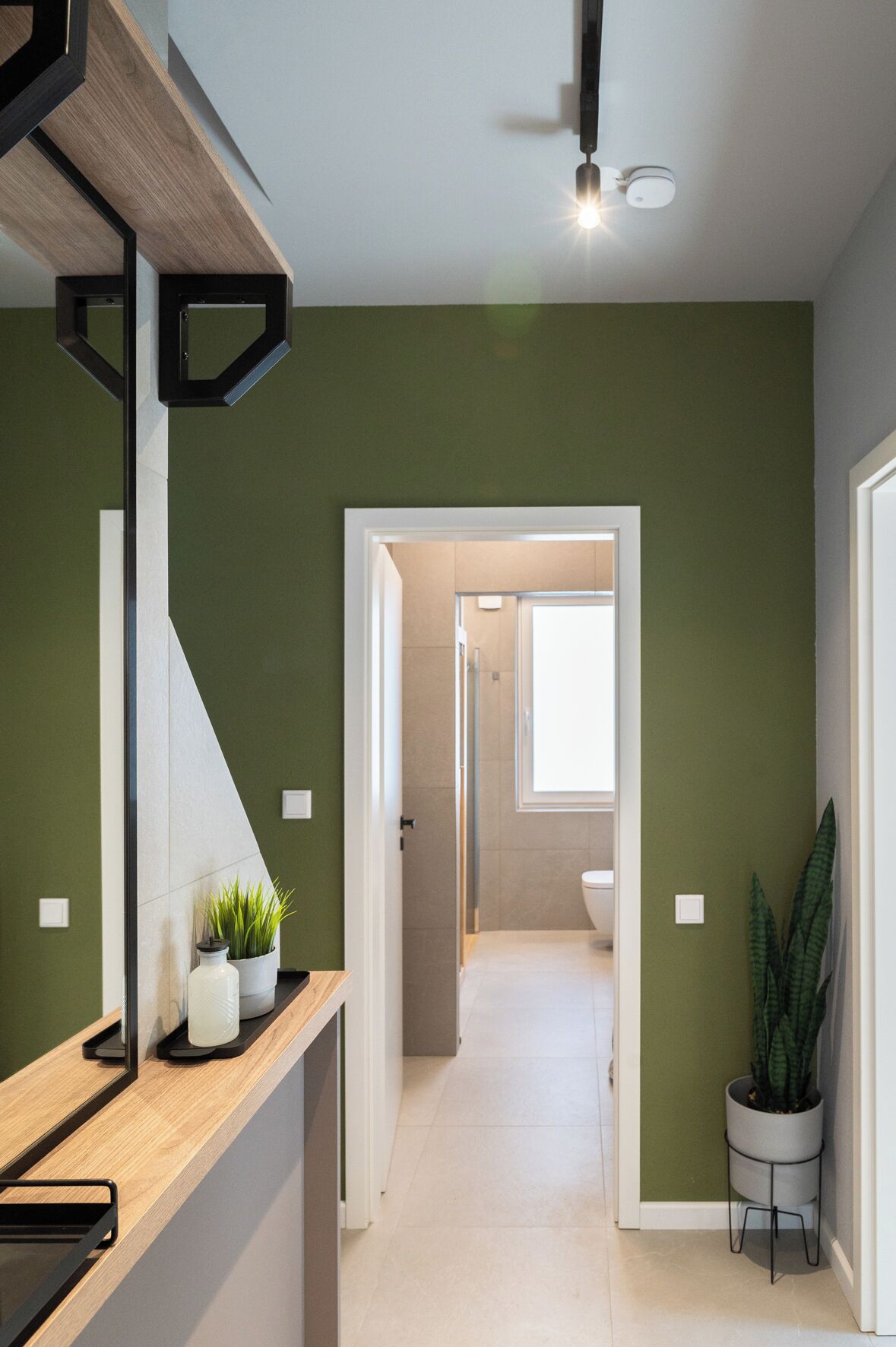 Passadís modern amb un taulell de fusta, plantes en testos i vista a un bany i una zona de cuina.