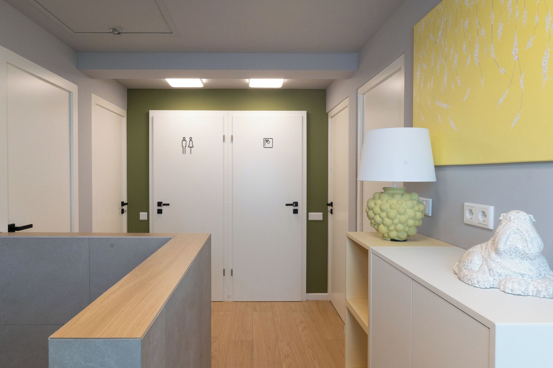 A hallway with a wooden reception desk, a lamp, and a sculpture.