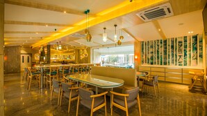 Un restaurant moderne avec un intérieur élégant, une longue table conviviale, plusieurs espaces de détente et une grande fenêtre ornée d’œuvres d’art.