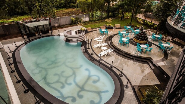 Une piscine entourée de verdure et agrémentée d’une petite fontaine, avec des chaises longues et des tables à proximité.